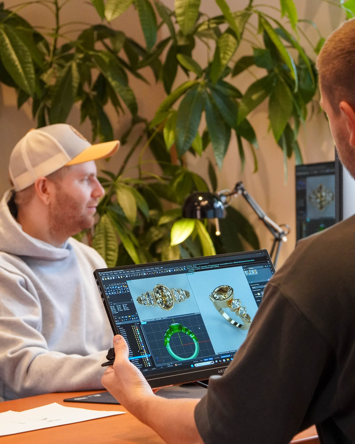 Two people working on a computer with jewelry design software in an office setting.