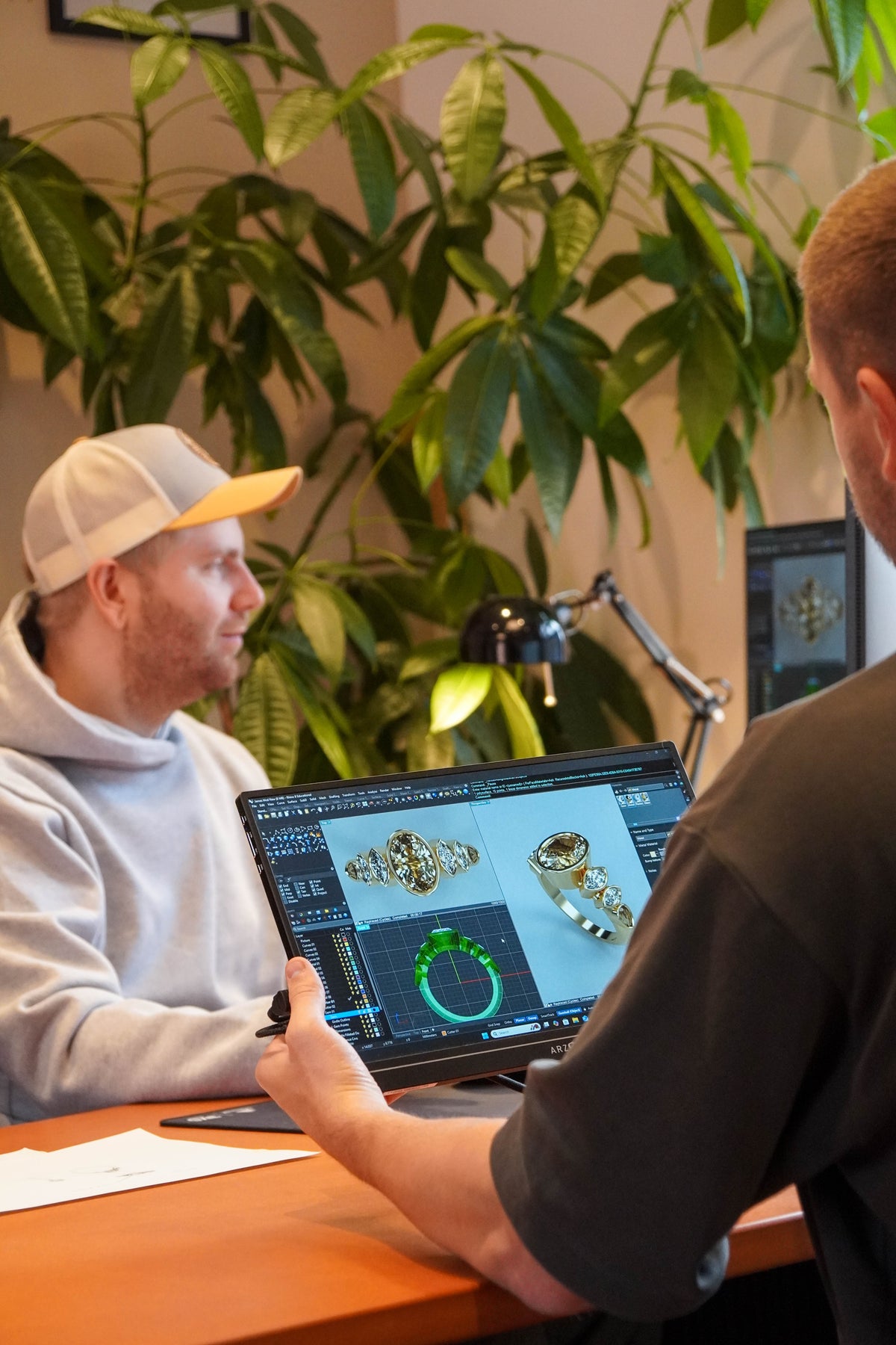 Two people working on a computer with jewelry design software in an office setting.