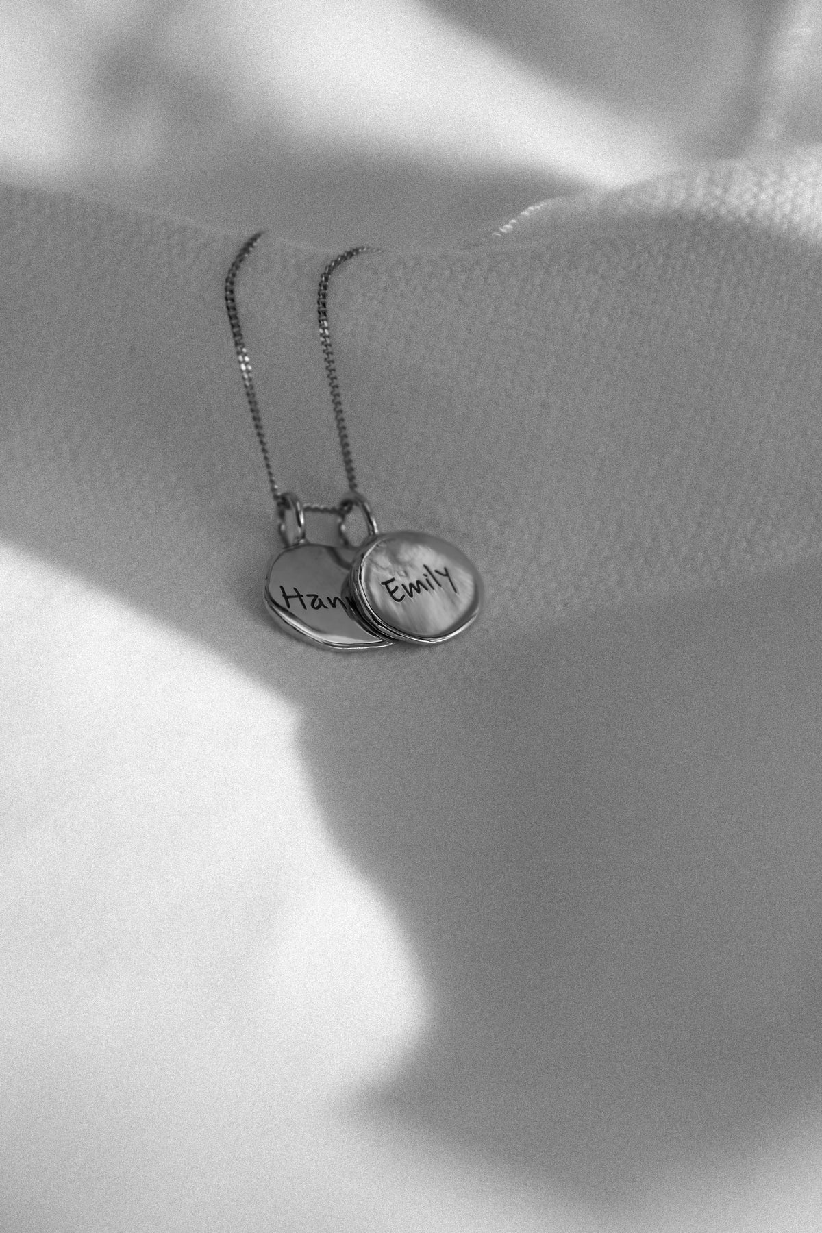 Worn: two silver fingerprint pendants engraved with names, on white fabric