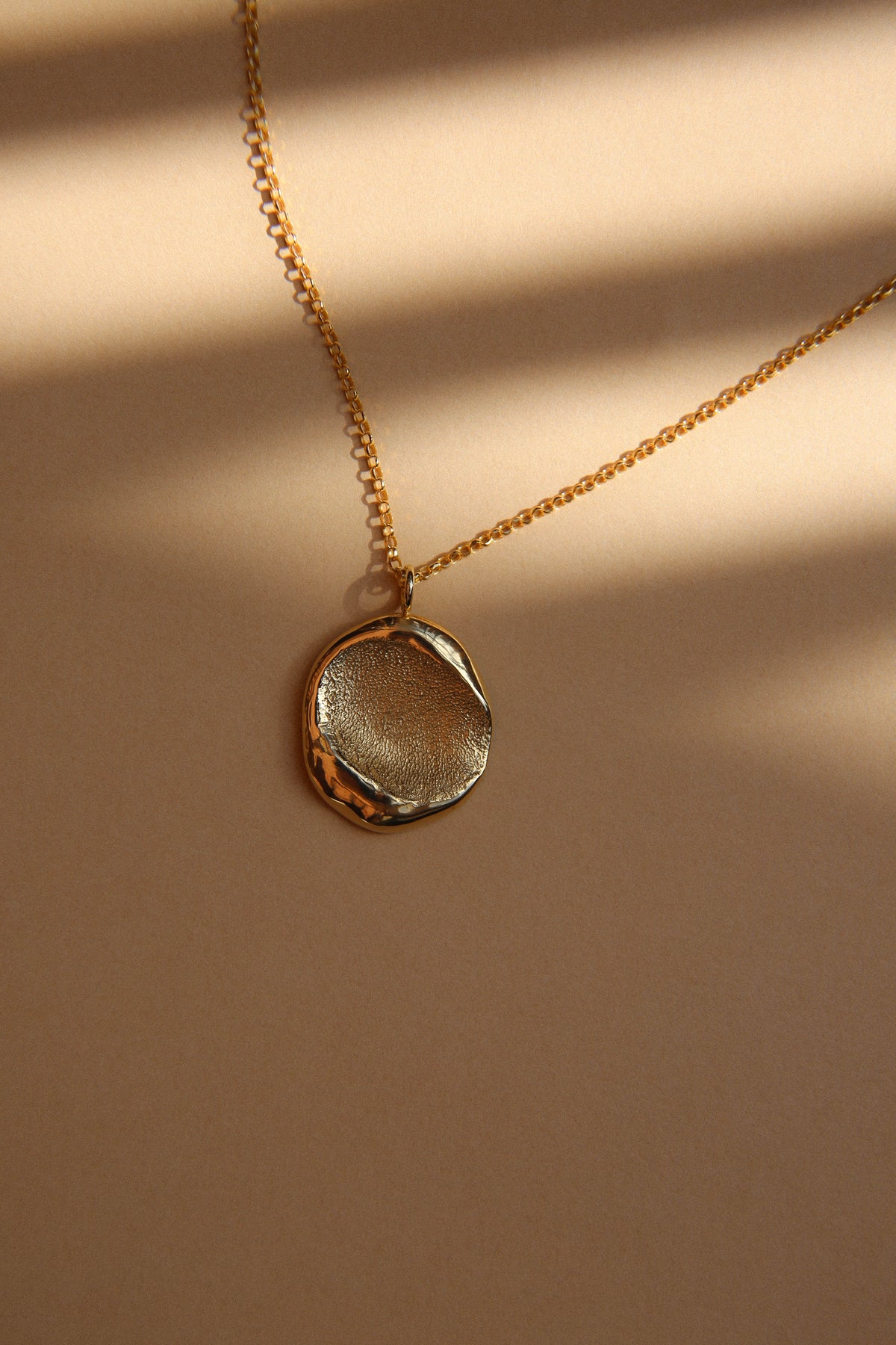 The details: gold fingerprint pendant on a chain, in stripes of sunlight